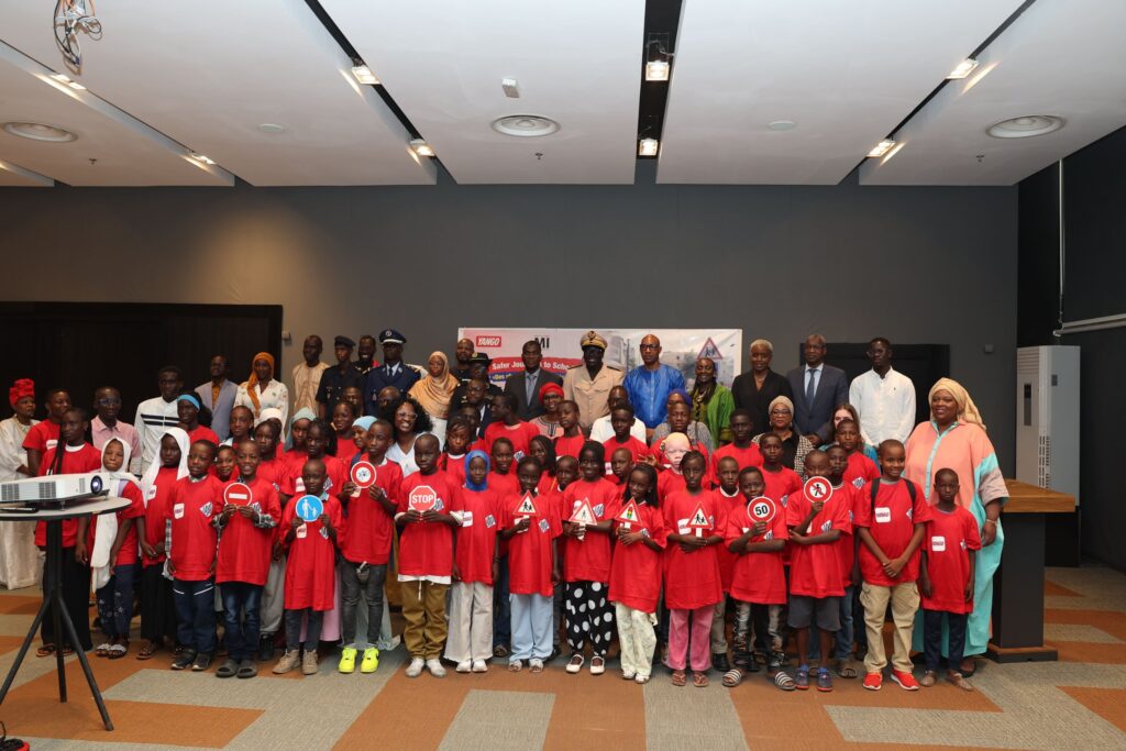 Élèves en t-shirts rouges tenant des panneaux de signalisation, avec des officiels, lors de la cérémonie Safer Journeys to School à Dakar